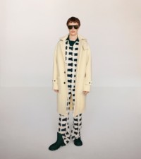 Modelo usando um duffle coat com capuz de lã em flor de narciso, com uma camisa de rugby de viscose e calças de lã em Sherbet e Ivy.