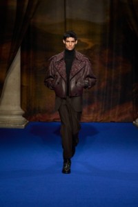 Nakul Bhardwaj indossa un trench in pelle con fiori ricamati berry purple, un pullover a collo alto in cashmere walnut brown, pantaloni sartoriali in lana bark brown e stivali in pelle nera.