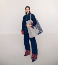 Modelo usando jaqueta e calças jeans em azul índigo, com uma bolsa tote com estampa EKD em knight e mules de shearling com bico fino em espresso escuro.