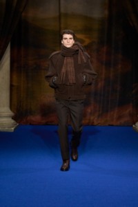 Ben Sherrell indossa una giacca con sciarpa in alpaca ginger brown, top in alpaca a coste beige mélange abbinato a pantaloni sartoriali soot brown e stivali Ledger in pelle treacle brown. 