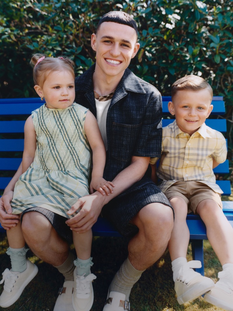 Phil Foden sat on blue bench with his children, wearing the Check Trim Cotton Shirt 