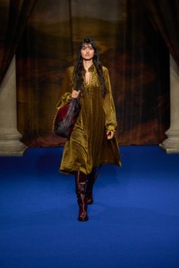 Neelam Gill indossa un abito geometrico in velluto jacquard pear yellow, stivali alti fino alla coscia in mahogany red, borsa a tracolla Highland in pelle fig purple, abbinata al bracciale con pendente Knight placcato oro e all'anello hollow.