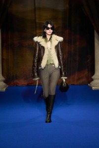 Hyun Seo indossa una giacca da aviatore in marrone scuro, top in velluto cricket yellow e pantaloni jodphur olive beige, abbinati a una borsa Knight Arc in pelle con pieghe peat brown.
