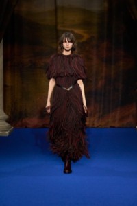 Lucy Fletcher indossa un abito in viscosa marrone, arancione e nero e stivali cavalier in pelle rosso mogano.